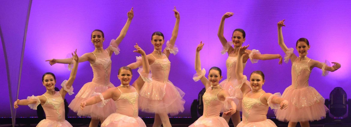 Eight young female ballerinas on stage posing.